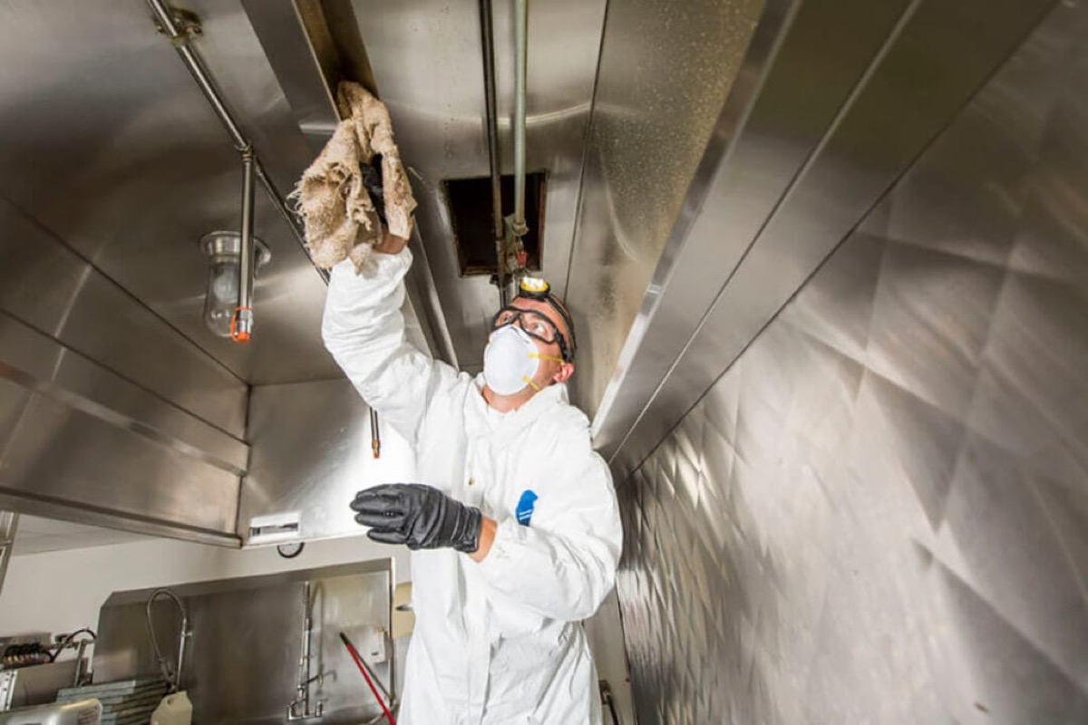 Technician cleaning inside a commercial kitchen hood